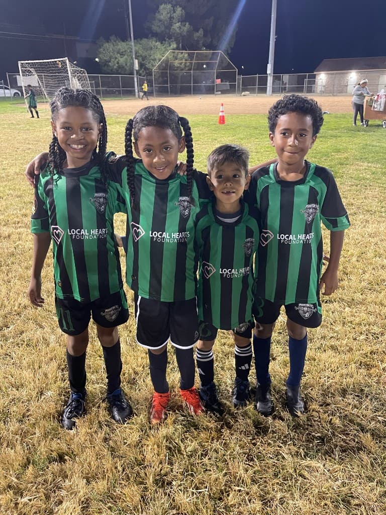 U7 Sparks teammates smiling together in Phantom FC and Local Hearts Foundation kits under the stadium lights