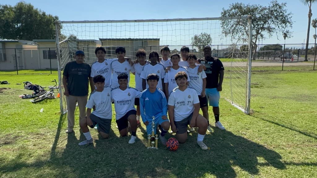 Youth squad and coaches posing with a gold trophy and soccer ball in front of the goal